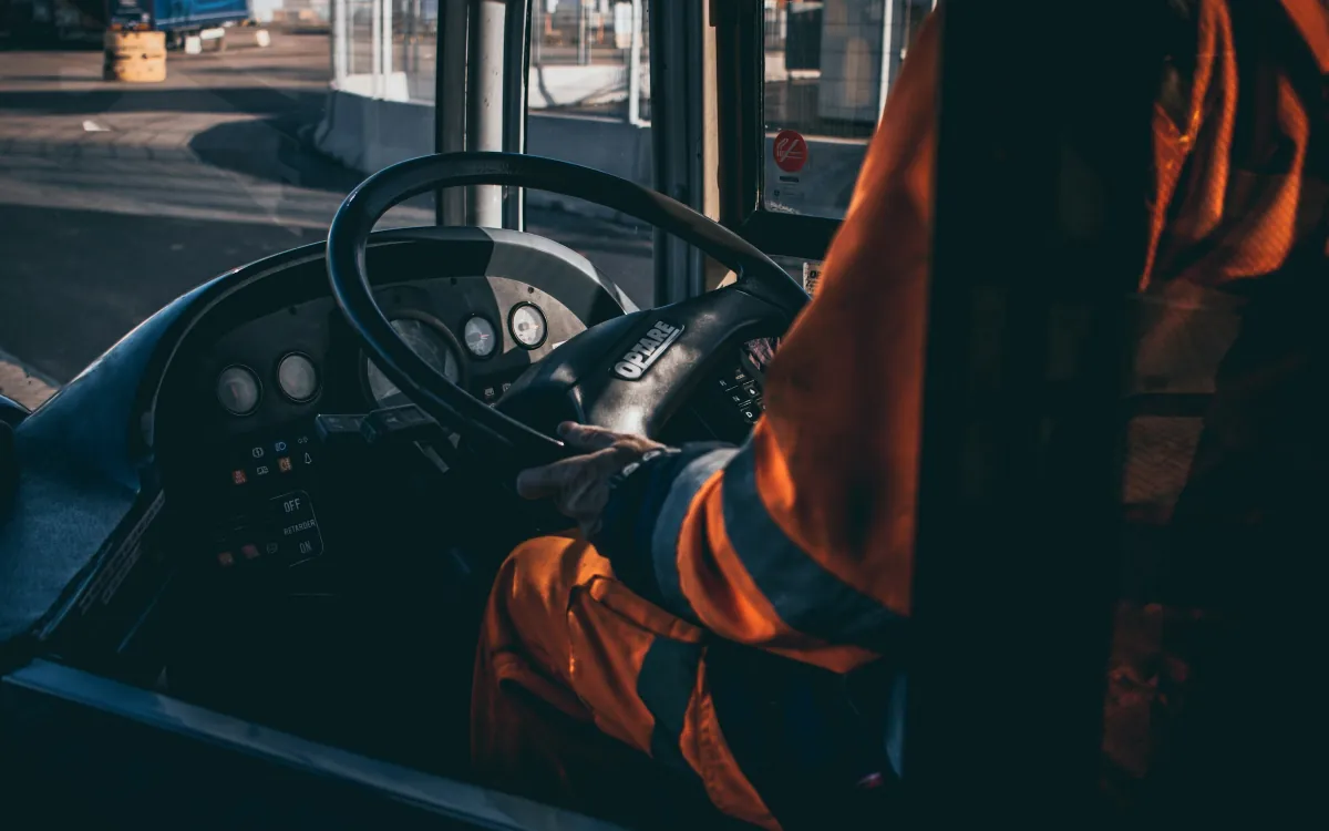Un șofer în haine de lucru ține volanul, fața nu se vede