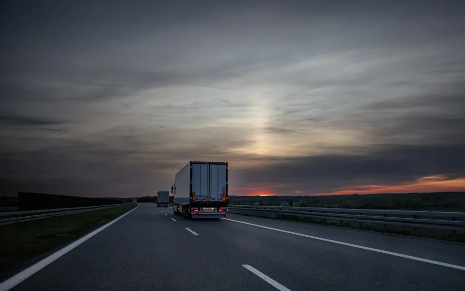 Camioane cu semiremorci pe autostradă, după apusul soarelui