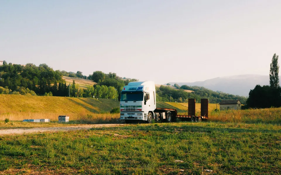 Un cap tractor cu semiremorcă cu platformă joasă stă pe un teren, printre câmpuri