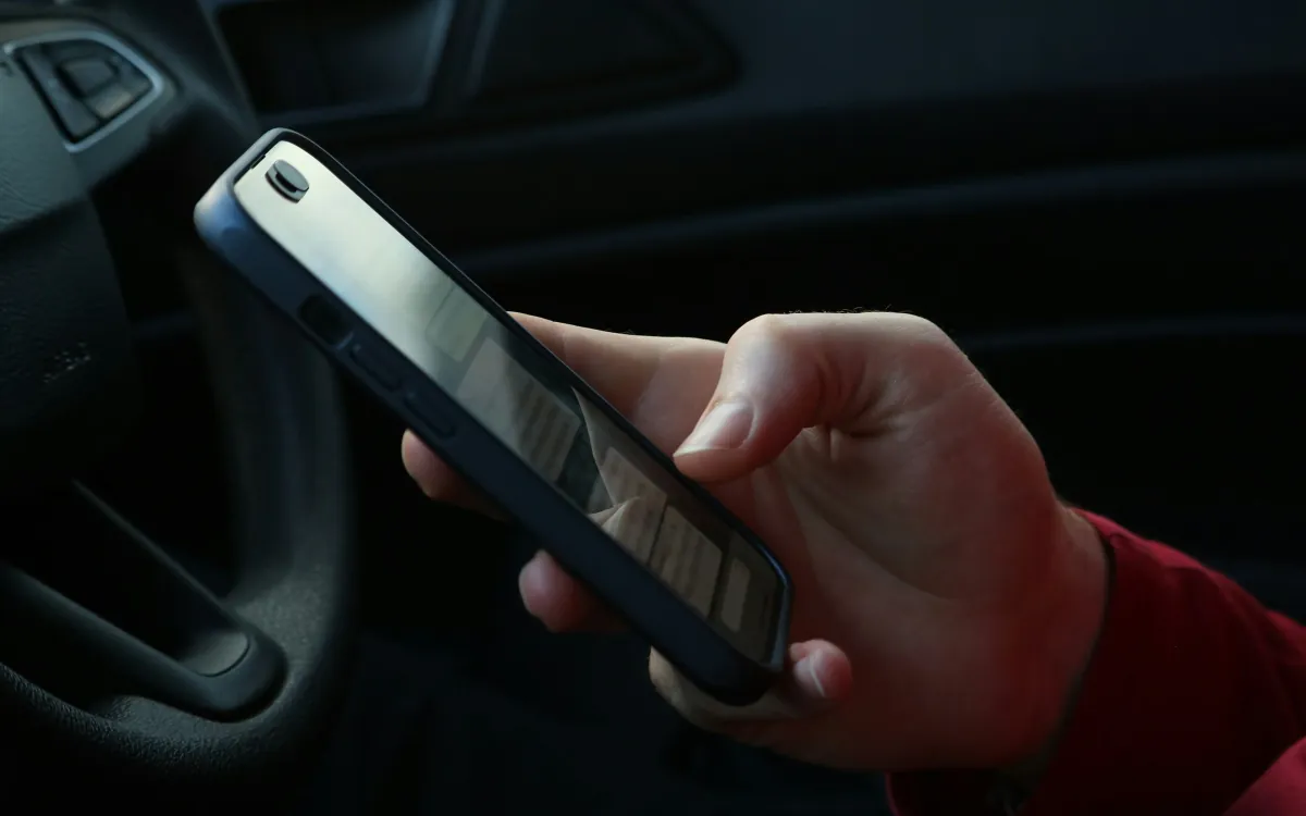 O mână cu telefonul lângă volan, fața nu se vede