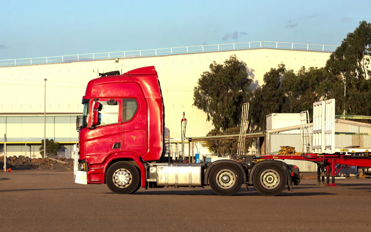 Un cap tractor roșu fără semiremorcă pe platforma de lângă un depozit