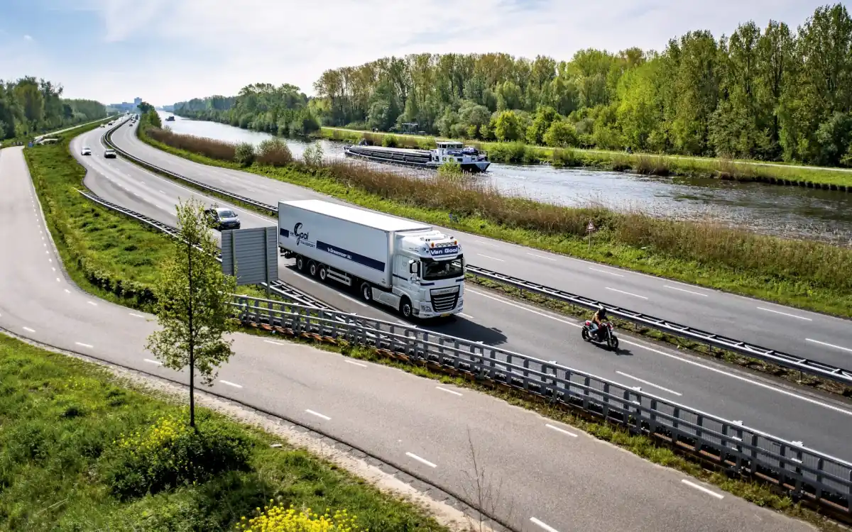 Un cap tractor cu semiremorcă merge pe o șosea de-a lungul unui canal