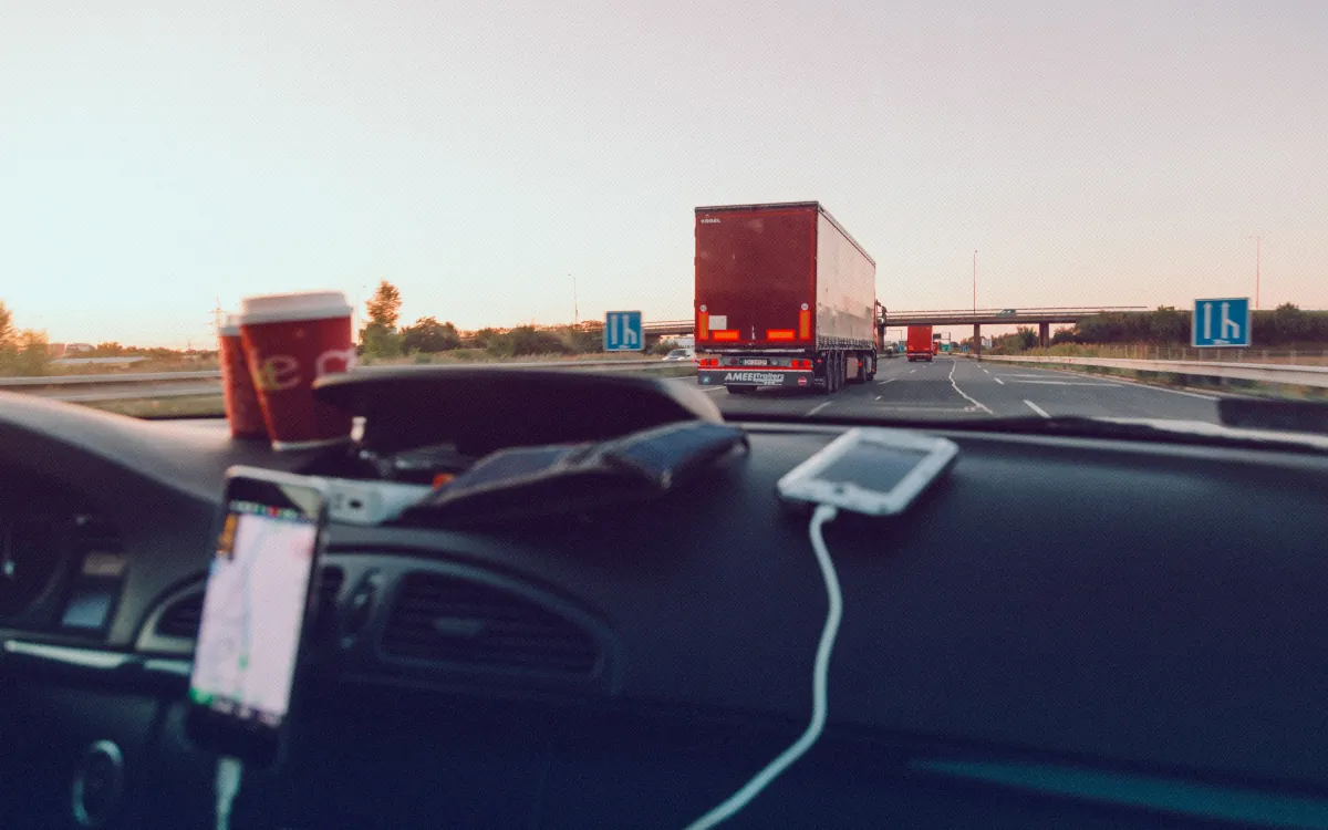 Vedere de la volan spre autostradă: în față un camion, pe bord un telefon cu hartă